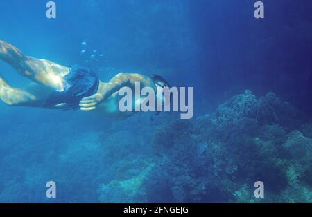 Mann, der in tiefblauem Meer taucht. Junger Schnorchel schwimmt unter Wasser. Männlicher Schnorchel im Unterwasserfoto der tropischen Lagune. Freitauchen im Korallenriff. Aktiver Sommer h Stockfoto