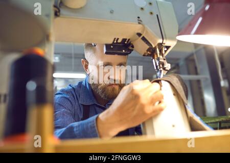 Mann, der am Tisch mit der Industrienähmaschine am Schuh arbeitet Oder die Fabrik für die Herstellung von Kleidung Stockfoto