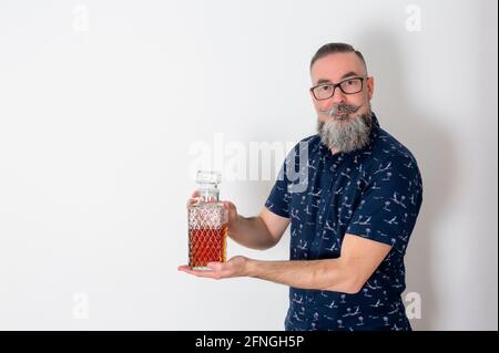 Retro-Look Hipster mit großem Bart und Brille, 40-45 Jahre alt, kaukasisch, hält alte Alkoholflasche und schaut geradeaus. Stockfoto