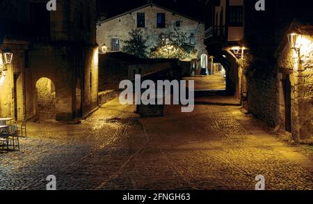 Nachtfoto einer einsamen Gasse aus dem Mittelalter mit Kopfsteinpflaster und Steinmauern in der schönen kantabrischen Stadt Santillana del Mar Stockfoto