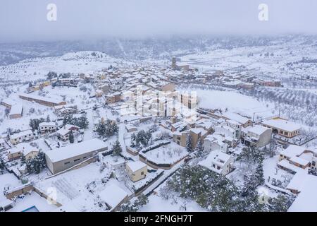 Luftaufnahme des Dorfes Ulldemolins und seiner Umgebung von Olivenhainen und Obstbäumen während eines Schneefalls (Priorat, Tarragona, Katalonien) Stockfoto