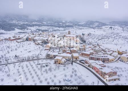 Luftaufnahme des Dorfes Ulldemolins und seiner Umgebung von Olivenhainen und Obstbäumen während eines Schneefalls (Priorat, Tarragona, Katalonien) Stockfoto