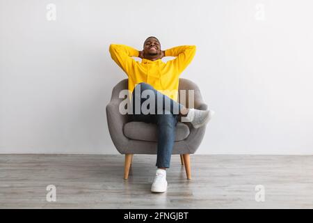 Afroamerikanischer Mann Entspannt Sitzen In Bequemen Sessel, Grauer Hintergrund Stockfoto