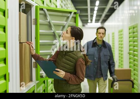 Junge Frau Checkboxen mit Mann, der sie in der trägt Hintergrund Sie arbeiten im Lager Stockfoto
