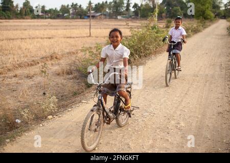 Don Det, Laos - 5. April 2013: Schulmädchen, die auf unbefestigten Straßen Fahrrad fahren. Stockfoto