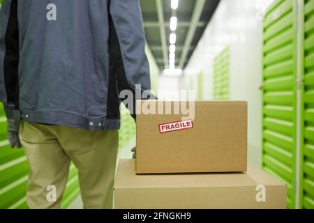 Rückansicht des Mannes, der Kartons auf dem Wagen trägt Das Lager Stockfoto