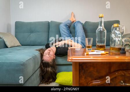 Betrunkene junge dunkelhaarige Frau schläft nach einer Party auf der Couch, leere Flaschen liegen auf dem Tisch Stockfoto