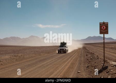 Vor dem Hintergrund von Vulkanen fährt ein Geländewagen im Geländewagen auf einer Touristensafari über Land durch die Wüstenlandschaft Boliviens. Stockfoto