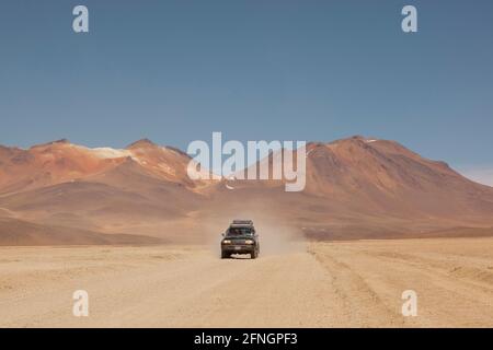 Vor dem Hintergrund von Vulkanen fährt ein Geländewagen im Geländewagen auf einer Touristensafari über Land durch die Wüstenlandschaft Boliviens. Stockfoto