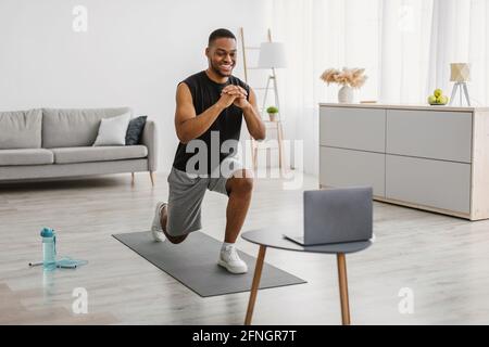 Afrikanischer Mann Tut Vorwärts Ausfallschritt Übung Beobachten Online-Workout Indoor Stockfoto