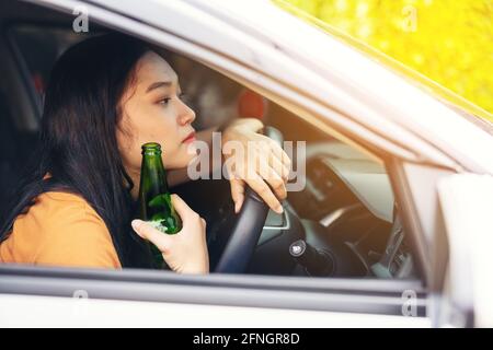 Frau trinkt aus einer Bierflasche während der Fahrt mit dem Auto, ein Konzept des Fahrens berauscht Stockfoto