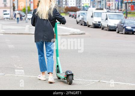 Das moderne Konzept des mobilen Elektrotransportes: Ein junges Mädchen steht mit einem Elektroroller auf dem Bürgersteig. Stockfoto