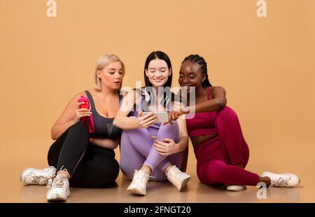 Fitness-Tracking-App Drei Multiethnische Frauen In Sportswear, Die Zusammen Smartphone Verwenden Stockfoto