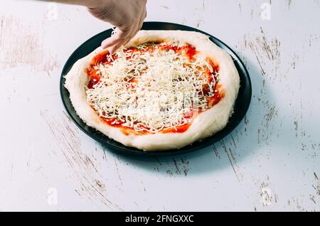 Der Koch bereitet eine hausgemachte Pizza zu, indem er Mozzarella darauf setzt Der Pizza mit Tomatensauce Stockfoto