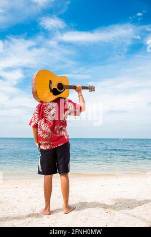 Schöner Mann, der am Strand mit blauem Himmel Gitarre spielt. Reisekonzept. Stockfoto