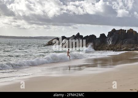 Morgenansicht des porthgwidden Strandes an einem bewölkten Tag mit Eine Frau, die aus dem Wasser auftaucht, nachdem sie mit einem Bikini geschwommen war Und Handschuhe Stockfoto