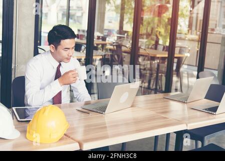 Asiatische stattlichen Geschäftsmanns, der outdoor im Coffee Shop mit Laptop und die Tasse Kaffee in der Hand. Arbeit außerhalb der Verwendung mit Technologie Stockfoto