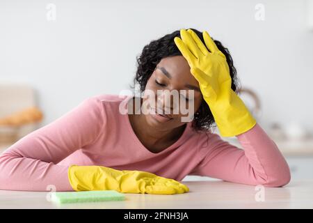 Müde schwarze Dame in Handschuhen hält Schwamm, schlief ein Stockfoto