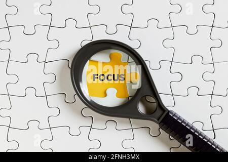 Das Wort Fokus auf fehlende Puzzle-Stück mit einer Lupe. Um ein Motiv zu fokussieren oder sich auf es zu konzentrieren. Stockfoto