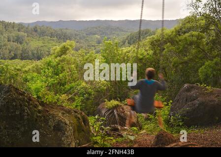 Frau, die auf einer Seilschaukel am Baum sitzt, auf dem Hügel der Gunstock Ranch, bei Sonnenuntergang, Laie, Oahu, Hawaii, USA Stockfoto