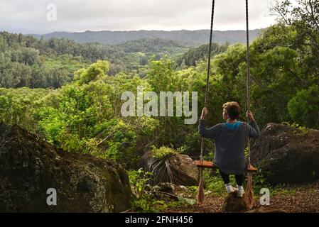 Frau, die auf einer Seilschaukel am Baum sitzt, auf dem Hügel der Gunstock Ranch, bei Sonnenuntergang, Laie, Oahu, Hawaii, USA Stockfoto