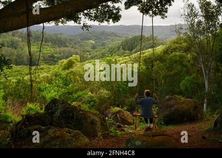 Frau, die auf einer Seilschaukel am Baum sitzt, auf dem Hügel der Gunstock Ranch, bei Sonnenuntergang, Laie, Oahu, Hawaii, USA Stockfoto