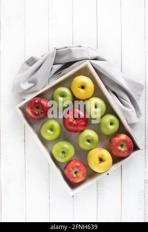 Bunte Äpfel in einem weißen Holztablett auf einem weißen Tabellenansicht von oben Stockfoto