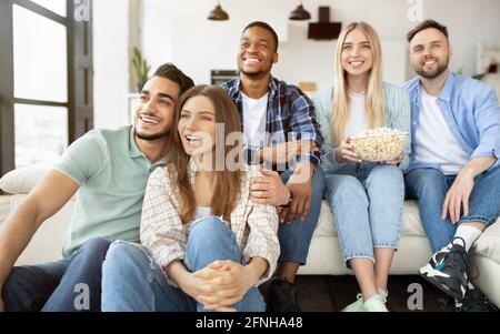 Eine Gruppe fröhlicher junger Freunde, die zu Hause einen Film genießen, Popcorn essen und lächeln Stockfoto