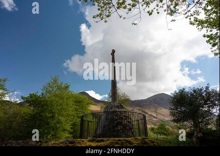 Glencoe Massacre Gedenkkreuz im Dorf Glencoe, Schottische Highlands an einem sonnigen Tag mit blauem Himmel und Wolken. Stockfoto