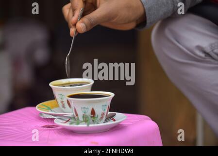 Addis Abeba. Mai 2021. Ein Kunde rührt Kaffee in einem Straßencafe in Addis Abeba, Äthiopien, am 14. Mai 2021. Äthiopien wird oft als die Geburtsstätte des Kaffees bezeichnet, während die traditionelle Kaffezeremonie, die ausschließlich die natürliche Verarbeitungsmethode beinhaltet, ein integraler Bestandteil der äthiopischen Gesellschaft ist. DAZU kommt: "Feature: Wachsende Zahl junger äthiopischer Frauen nutzen traditionellen Kaffee als lebensfähige Einkommensquelle" Kredit: Michael Tewelde/Xinhua/Alamy Live News Stockfoto