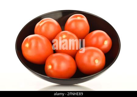 Mehrere leuchtend rote saftige Tomaten mit schwarzer Keramikplatte, Nahaufnahme, auf weißem Hintergrund. Stockfoto