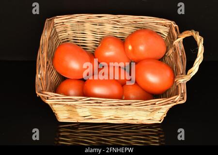 Mehrere reife rote Tomaten in einem Weidenkorb, Nahaufnahme, auf schwarzem Hintergrund. Stockfoto