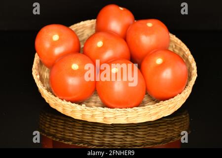 Mehrere reife rote Tomaten auf einem Strohteller, Nahaufnahme, auf schwarzem Hintergrund. Stockfoto