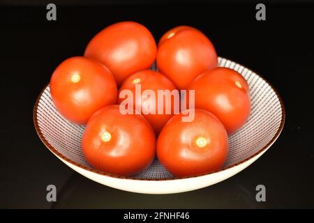 Mehrere reife rote Tomaten mit Keramikplatte, Nahaufnahme, auf schwarzem Hintergrund. Stockfoto