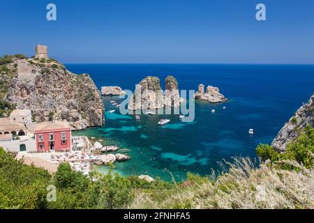 Scopello, Trapani, Sizilien, Italien. Blick über die felsige Bucht auf die Faraglioni, eine Reihe von Schornsteinen im Golf von Castellammare vor dem Tonnara di Scopello. Stockfoto