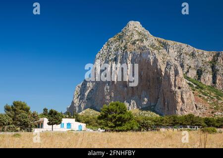 San Vito Lo Capo, Trapani, Sizilien, Italien. Isoliertes Dorfhaus, das von der aufragenden Nordwand des Monte Monaco in den Schatten gestellt wird. Stockfoto