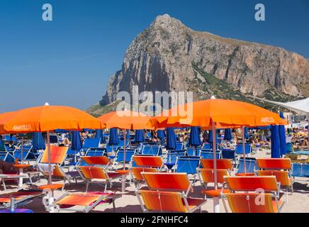 San Vito Lo Capo, Trapani, Sizilien, Italien. Auffällige Strandmöbel an überfüllter Küste, die aufragende Nordwand des Monte Monaco im Hintergrund. Stockfoto