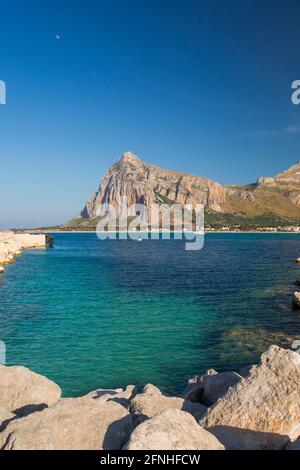 San Vito Lo Capo, Trapani, Sizilien, Italien. Blick vom Wellenbrecher über das klare türkisfarbene Wasser auf die aufragende Nordwand des Monte Monaco. Stockfoto