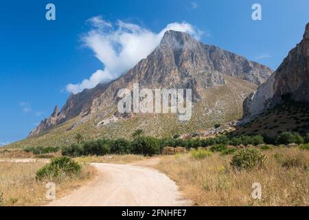 Custonaci, Trapani, Sizilien, Italien. Blick auf den staubigen Weg zwischen Feldern zur hoch aufragenden Südwand des Monte Cofano. Stockfoto