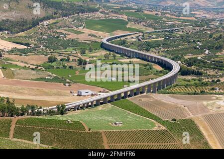 Calatafimi-Segesta, Trapani, Sizilien, Italien. Abgehängte Autobahn, die sich über attraktive Ackerflächen unterhalb des Monte Bàrbaro schlängelt, archäologische Stätte von Segesta. Stockfoto