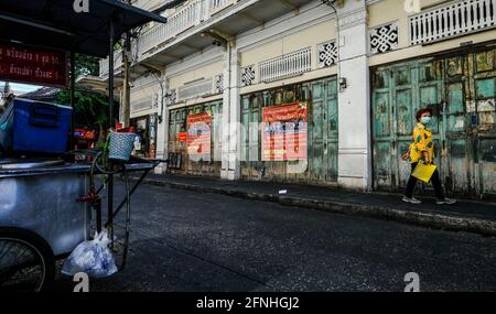 Eine Frau, die eine gelbe Decke trägt, geht an einer Reihe alter, grün verwitterter Türen vorbei, in der Nähe von Wat Mangkon in Bangkok, Thailand Stockfoto