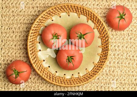 Mehrere saftige rosafarbene Tomaten auf einer Keramikplatte auf einer Strohmatte, Nahaufnahme, Draufsicht. Stockfoto