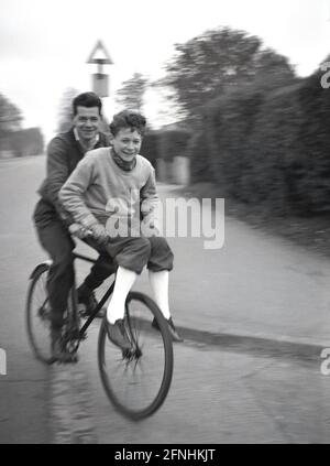 1954, historisch, draußen auf einer Straße, ein Mann auf seinem Fahrrad, der einem jungen Teenager in einer baggy-kneed Hose oder Knickerbockers, der auf dem vorderen Lenker sitzt, einen Aufzug gibt, England, Großbritannien. Stockfoto