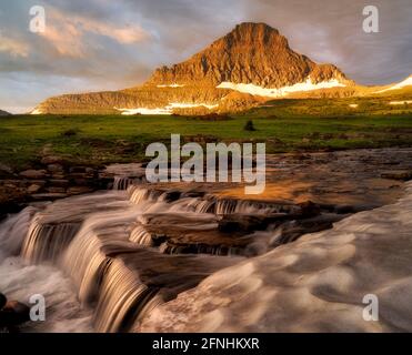 Wasserfall entlang Reynolds Creek am Logan Pass mit Mt. Reynolds und Snow Bank bei Sonnenaufgang, Glacier National Park, Montana Stockfoto