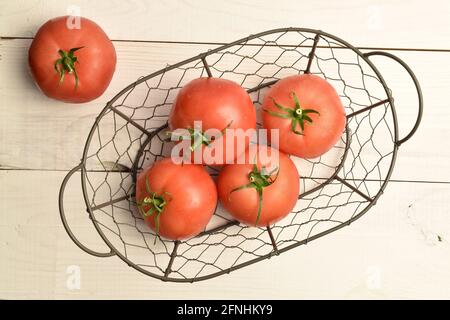 Mehrere reife rosa Tomaten in einem Korb, Nahaufnahme, auf einem weißen Holztisch, Draufsicht. Stockfoto