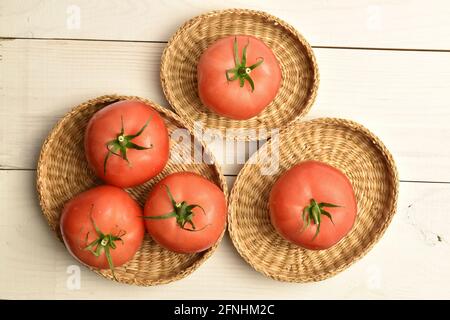 Mehrere reife rosa Tomaten in Strohtellern, Nahaufnahme, auf einem weißen Holztisch, Draufsicht. Stockfoto