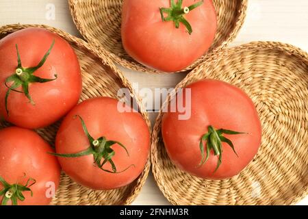 Mehrere reife rosa Tomaten in Strohtellern, Nahaufnahme, auf einem weißen Holztisch, Draufsicht. Stockfoto