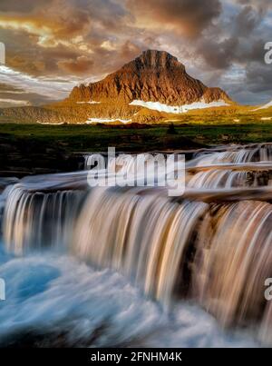 Wasserfall auf Reynolds Creek am Logan Pass mit Mt. Reynolds und Sonnenaufgang, Glacier National Park, Montana Stockfoto