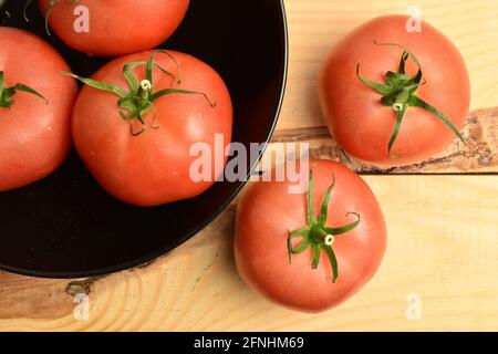 Mehrere reife rosafarbene Tomaten in einer schwarzen Keramikplatte, Nahaufnahme, auf einem Holztisch, Draufsicht. Stockfoto