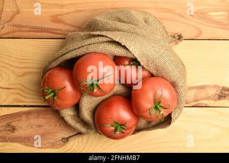 Mehrere saftige rosafarbene Tomaten im Jutebeutel, Nahaufnahme, auf einem Holztisch, Draufsicht. Stockfoto